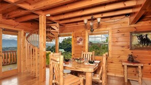 A wooden cabin interior with a dining table, chairs, a chandelier, a staircase, and a painting of a bear. - Mountain Splendor: Best Mountain View in Starr Crest Resort - Brand New Hot Tub (Sevierville)