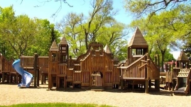 Een houten speelconstructie met meerdere glijbanen en klimmogelijkheden, omringd door bomen.