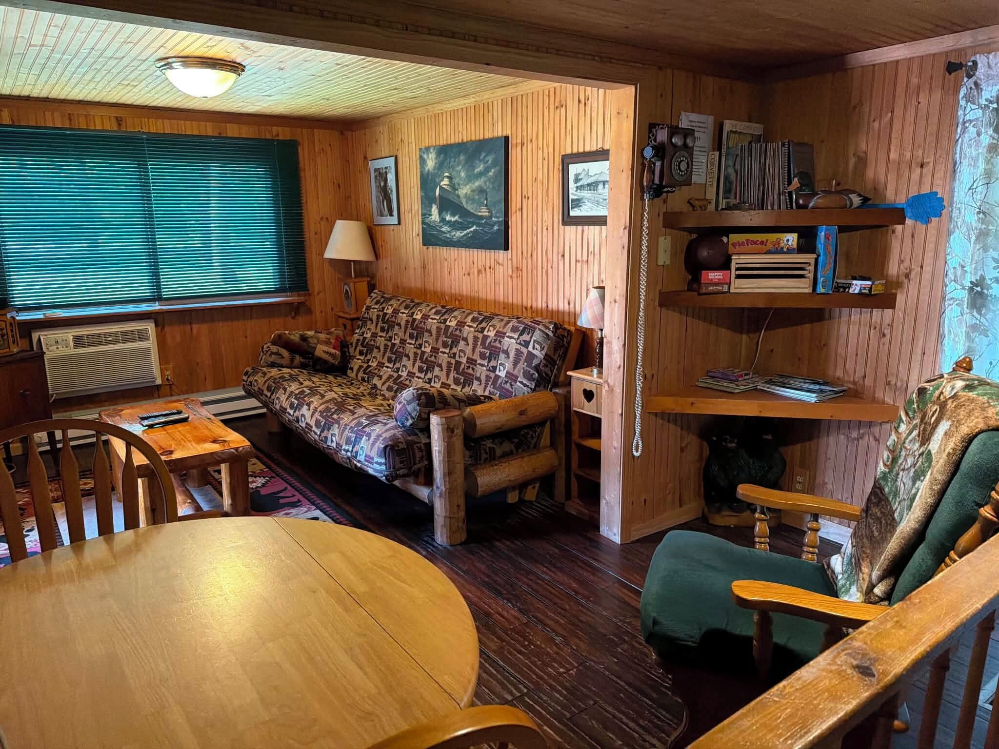 A cozy cabin interior with a wooden floor, a sofa, a dining table, and a bookshelf.