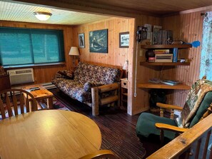 A cozy cabin interior with a wooden floor, a sofa, a dining table, and a bookshelf. - Black River Retreat-Dog Friendly! (Bessemer)