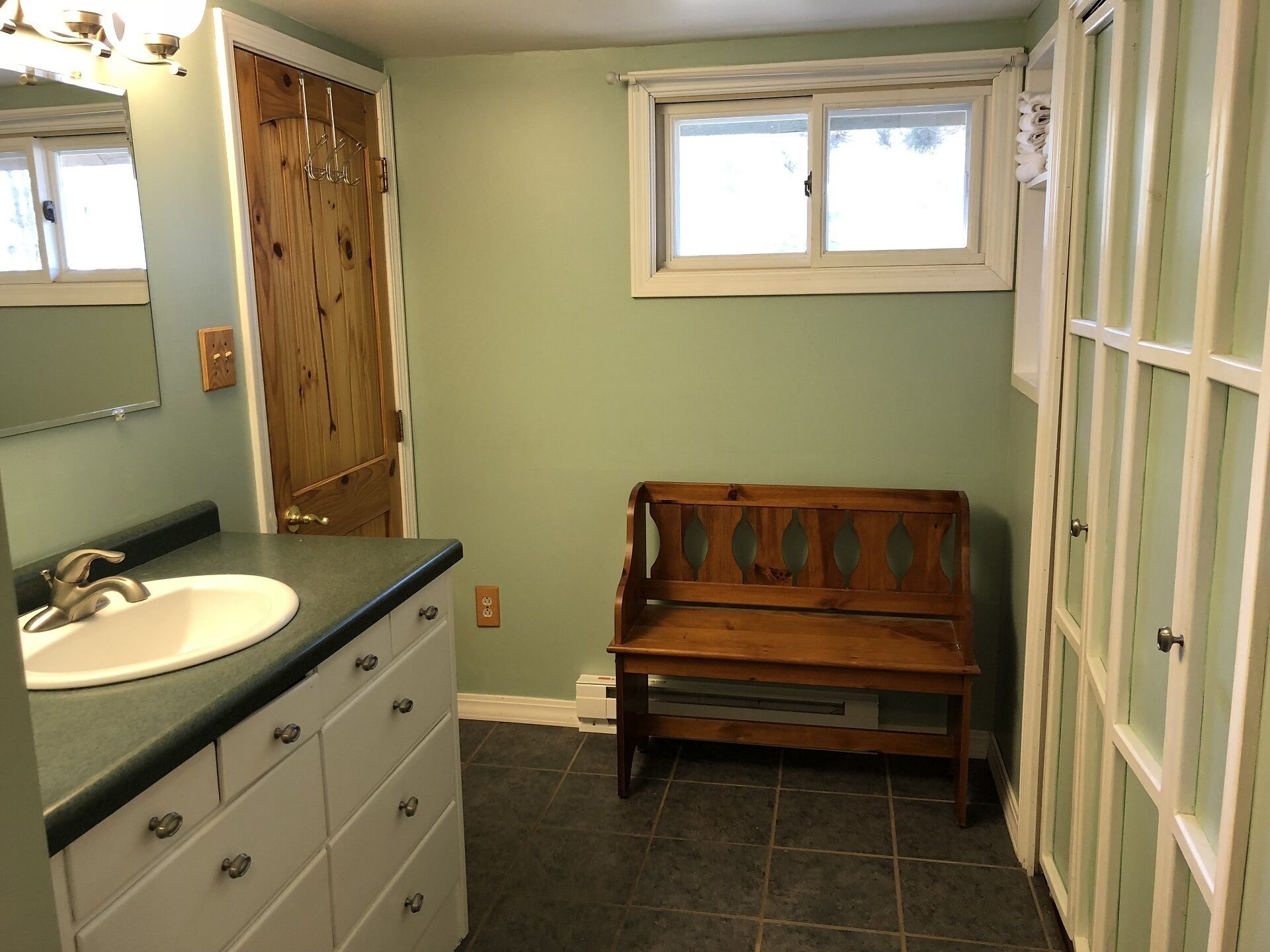 A bathroom with a wooden bench, a sink, and a window.