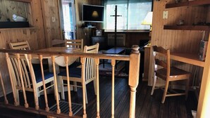 A wooden dining area with a table and chairs, a television, and a cross on the wall. - Black River Retreat-Dog Friendly! (Bessemer)