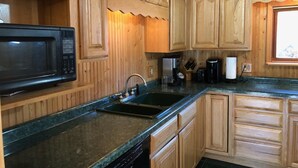 A kitchen with wooden cabinetry, a black microwave, a coffee maker, and a sink. - Black River Retreat-Dog Friendly! (Bessemer)