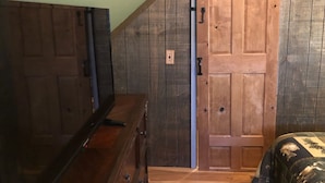 A room with a wooden sliding door, a dresser, and a bed with a camouflage cover. - Black River Retreat-Dog Friendly! (Bessemer)