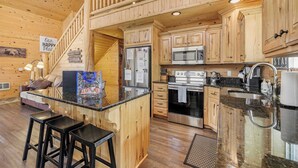 A wooden cabin interior with a kitchen, bar area, and a staircase.