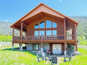 Eine zweistöckige Holzhütte mit Balkon, großen Fenstern und einem Rasen.