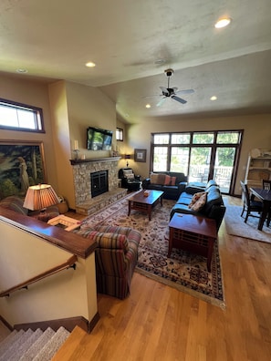A spacious living room with a fireplace, comfortable seating, a television, and large windows. - Pristine condo! Walking distance to everything in the heart of Fish Creek! (Fish Creek)
