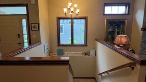 Una escalera con barandilla de madera, un candelabro y una ventana con vista a un edificio.