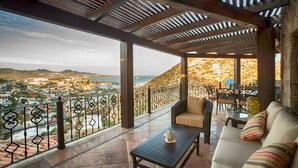 Un espace extérieur aménagé, abrité et doté d’une vue sur une ville côtière, avec un canapé, des fauteuils et une table.