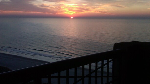 A sunset over a calm sea with a railing in the foreground. -  Beautiful Oceanview Margate. Book now for June and July (Myrtle Beach)