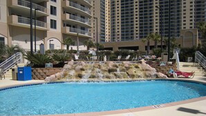 A swimming pool with a waterfall feature, surrounded by lounge chairs and a high-rise building in the background. -  Beautiful Oceanview Margate. Book now for June and July (Myrtle Beach)