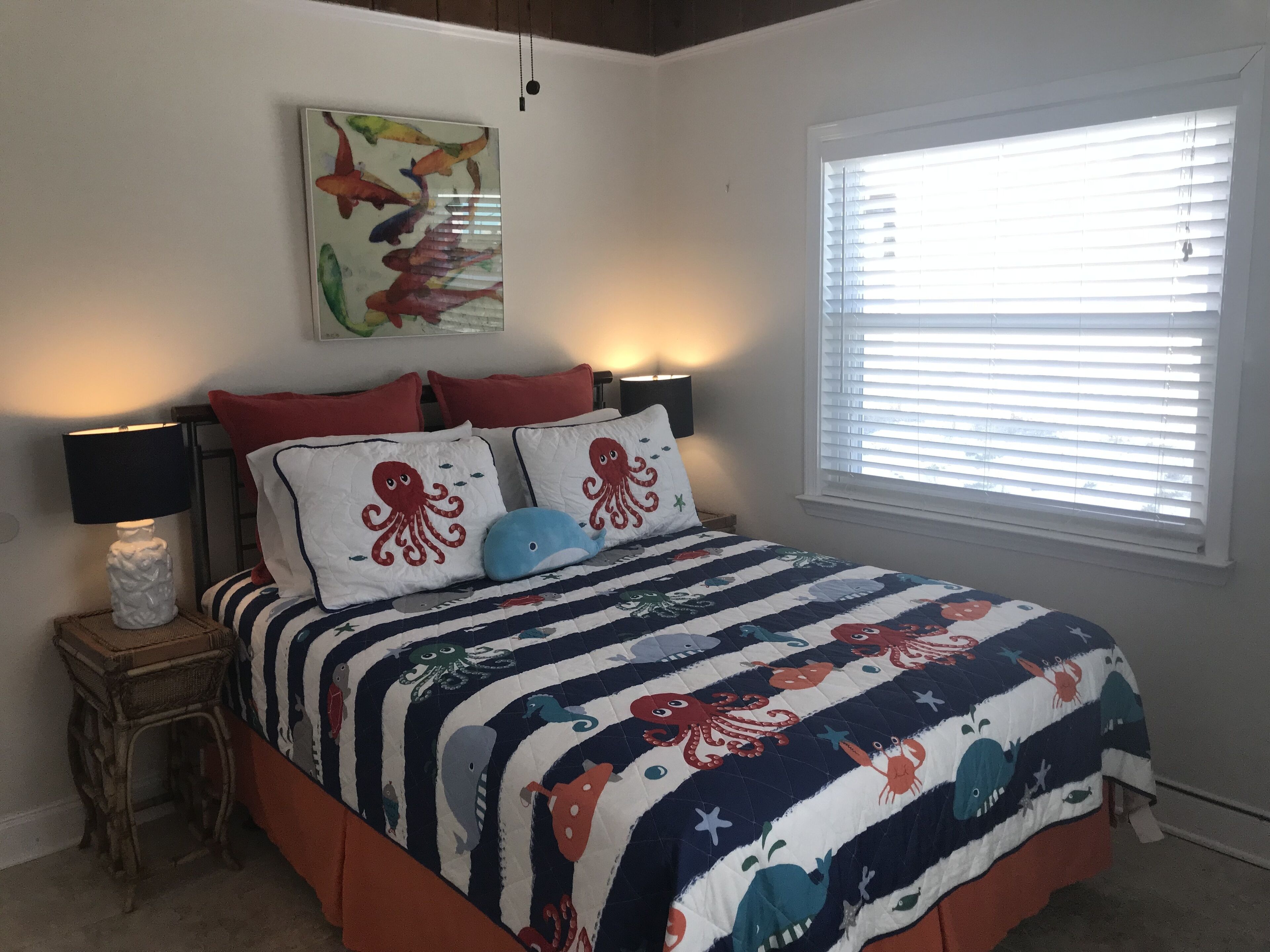 Una camera da letto con un letto, un comodino, una lampada, una finestra con persiane e un quadro appeso al muro.