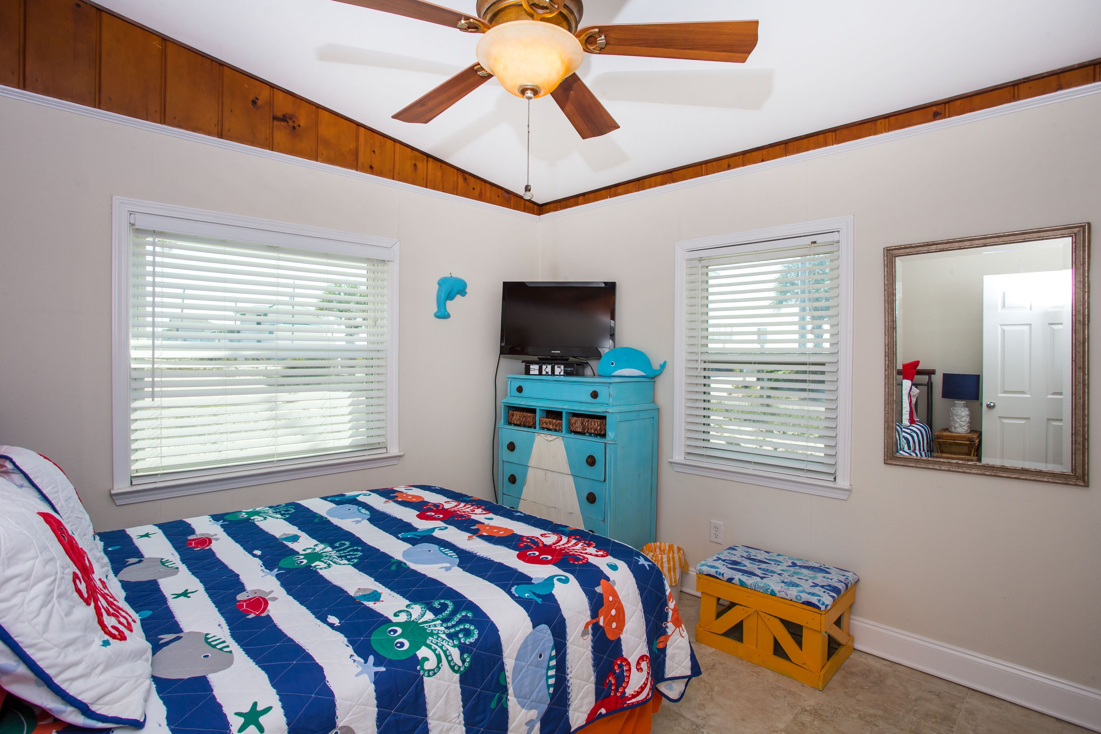 A bedroom with a bed, a ceiling fan, a TV, a dresser, and a window with blinds.