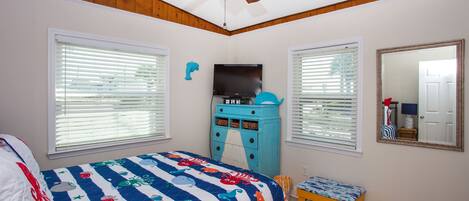 A bedroom with a bed, a ceiling fan, a TV, a dresser, and a window with blinds.