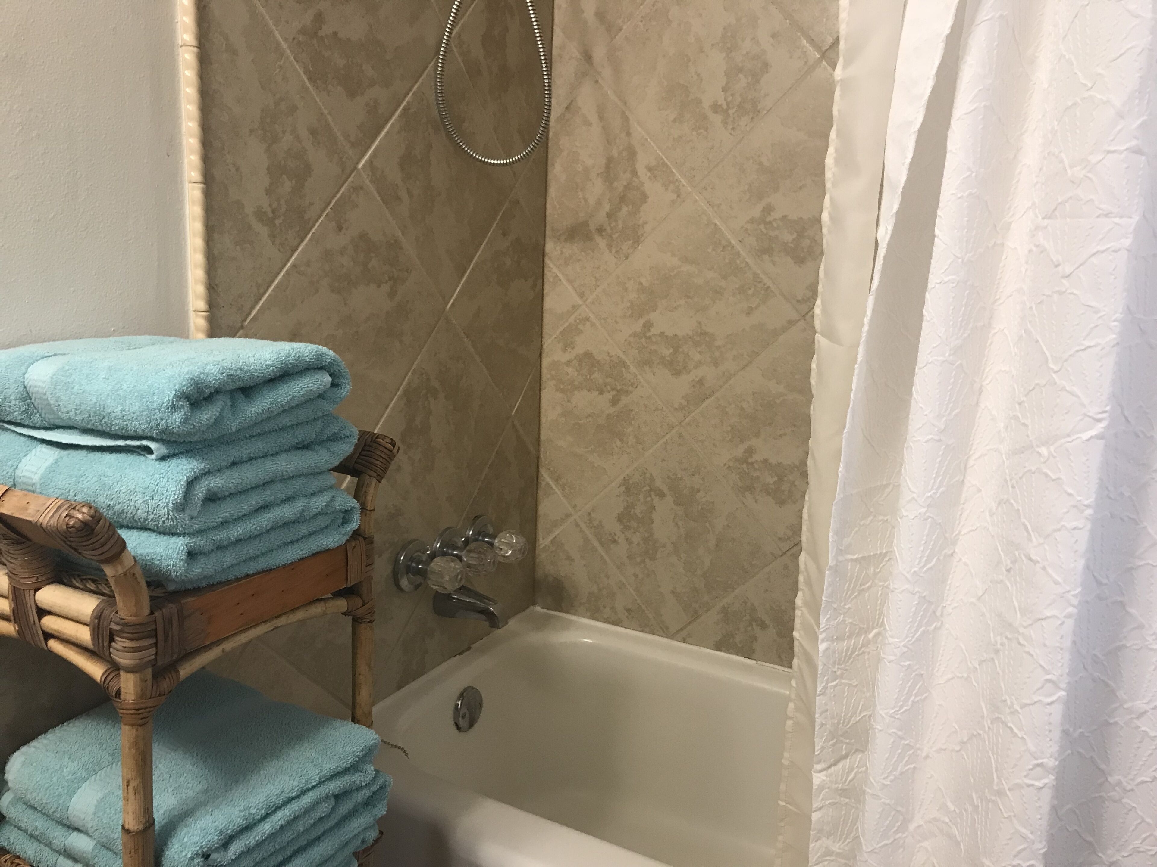 A bathroom with a bathtub, a wooden shelf holding towels, and a shower curtain.