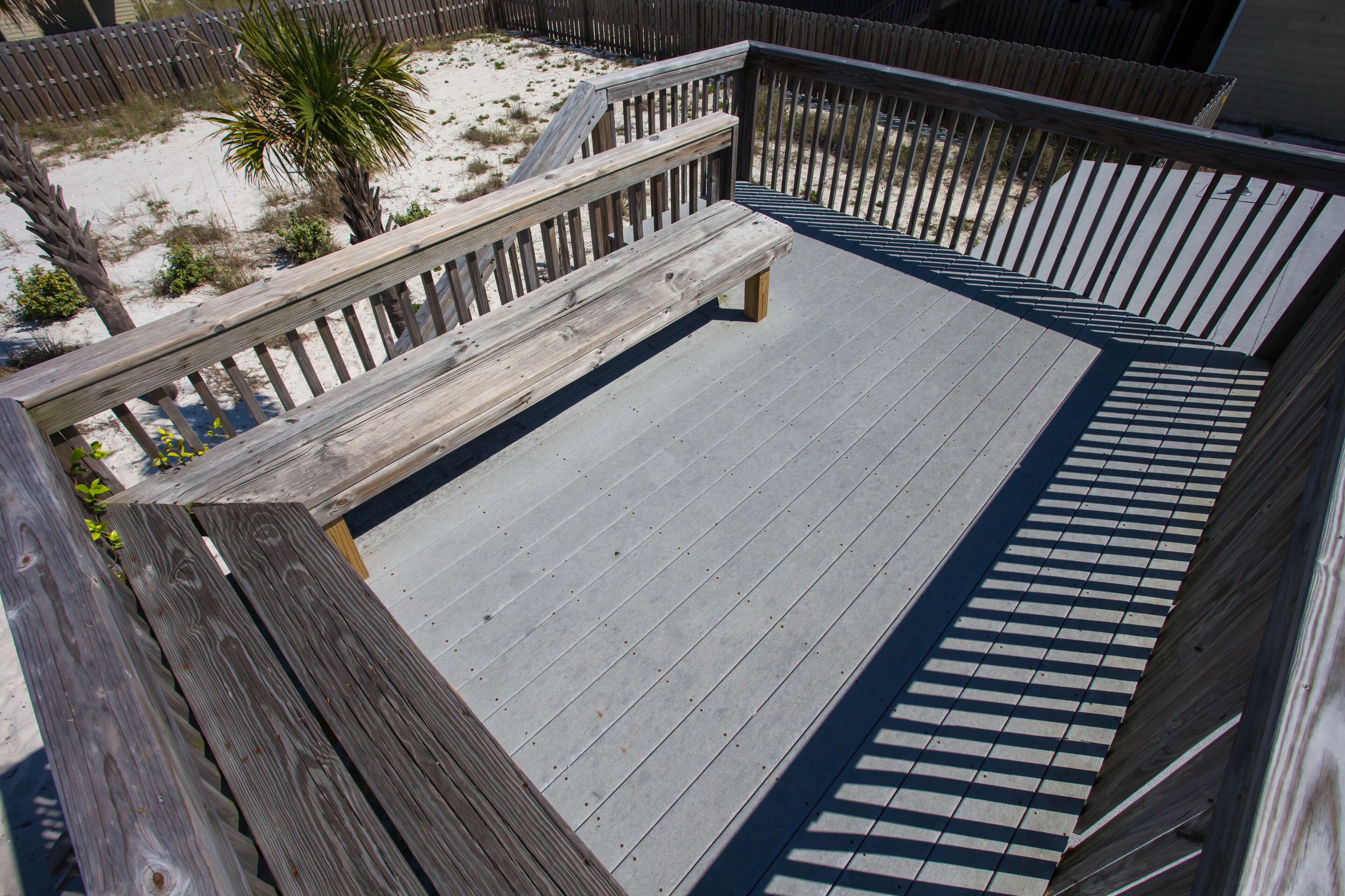 A wooden deck with a bench and a palm tree in the background.