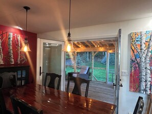 Un coin repas avec une table et des chaises en bois, une porte vitrée donnant sur l’extérieur et une vue sur un jardin.