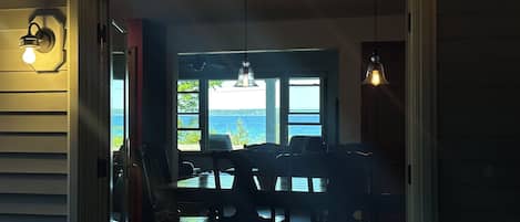 Een kamer met een eettafel en stoelen, uitzicht op de zee door grote ramen en een plafondventilator.