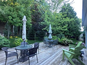 Une terrasse en bois, aménagée avec du mobilier d’extérieur, notamment une table ronde et des chaises, ainsi que deux parasols.