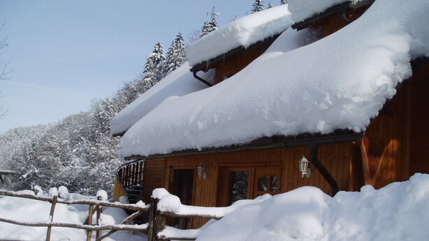 Een houten blokhut met een met sneeuw bedekte dak en een houten omheining ervoor.