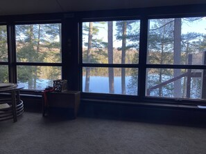 Guests can enjoy serene lake views from the large windows in this room, which features a carpeted floor and a small table with a chair.