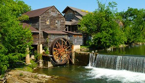 Un vieux moulin à eau, de style rustique, doté d’une grande roue en bois et surplombant une cascade.