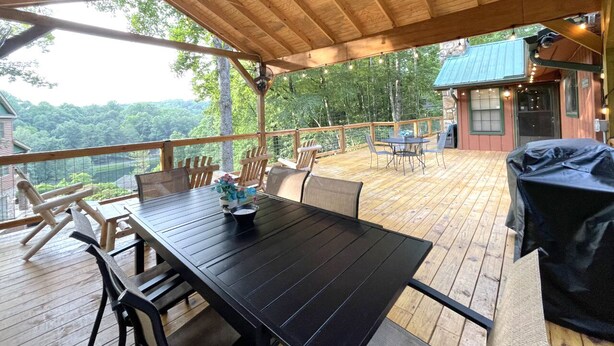 Una terraza techada al aire libre con una mesa y sillas de madera, una parrilla y vistas a un paisaje montañoso.