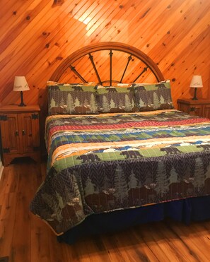Une chambre confortable avec un plafond en bois et un grand lit recouvert d’une couette aux couleurs vives. On y trouve deux tables de chevet avec des lampes.