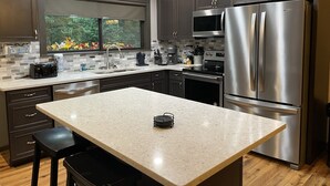 Una cocina moderna con armarios de madera oscura, electrodomésticos de acero inoxidable, una isla grande y un ventanal con vistas a árboles.