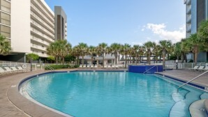 A swimming pool with lounge chairs and palm trees, surrounded by a building with a white facade and a blue-tiled pool edge. - Mainsail-On beach-Renovated 2BR/BA with 1 beach umbrella/chairs setup to Oct 31 (Destin)