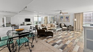 A modern living room with a glass dining table, wicker chairs, a sofa, and a ceiling fan. - Mainsail-On beach-Renovated 2BR/BA with 1 beach umbrella/chairs setup to Oct 31 (Destin)