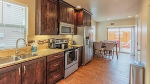 A kitchen with dark wooden cabinets, stainless steel appliances, a granite countertop, and a dining area with a table and chairs. - Townhome 4 in Springdale, at Zion National Park (Springdale)