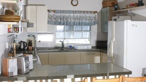 Una cocina con ventana, pileta, refrigerador y diversos electrodomésticos.
