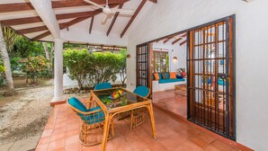 A covered patio with a table and chairs, a ceiling fan, and a view of a garden.