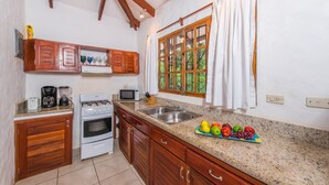 A kitchen with wooden cabinets, a stove, a microwave, and a sink. There is a window with curtains and a fruit bowl on the counter.