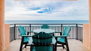A balcony with a view of the ocean, a table, and four chairs.