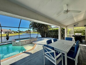 A pool area with a table and chairs, a ceiling fan, and a view of a lake and houses.