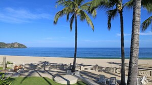 Vista de playa con palmeras, una zona arenosa con sillas de descanso y un cielo azul despejado.