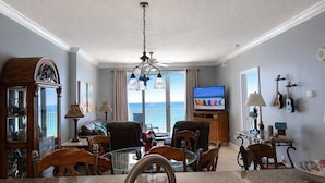 Uma sala de estar com televisão, um espaço de refeições com mesa e cadeiras, uma cozinha com pia e vista para o oceano.