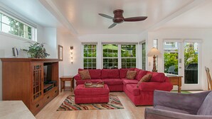 A spacious living room with a sectional sofa, a wooden entertainment center, and a ceiling fan. - Charming  2 Bedroom/2 Bath with Fireplace, Beach is 2 min Walk (San Diego)