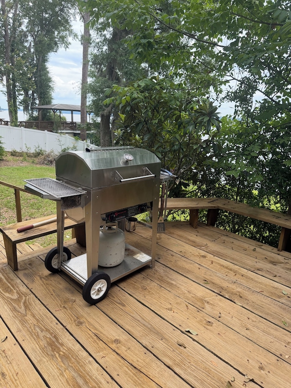 Una parrilla portátil en una terraza de madera con vista a un lago y árboles.