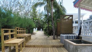 Une terrasse en bois avec des bancs, un bac à fleurs en béton planté, et une clôture blanche.