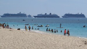 Une plage avec plusieurs navires de croisière en arrière-plan.