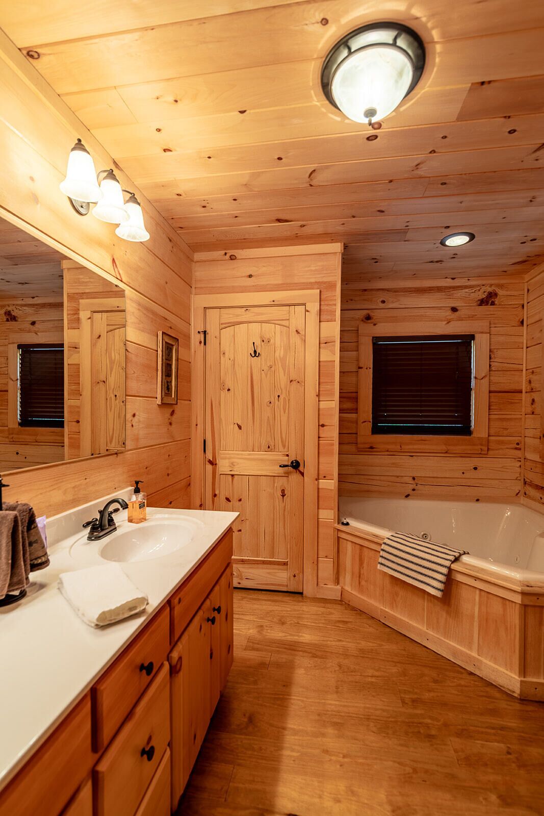 A wooden cabin bathroom with a sink, mirror, vanity, and a bathtub.