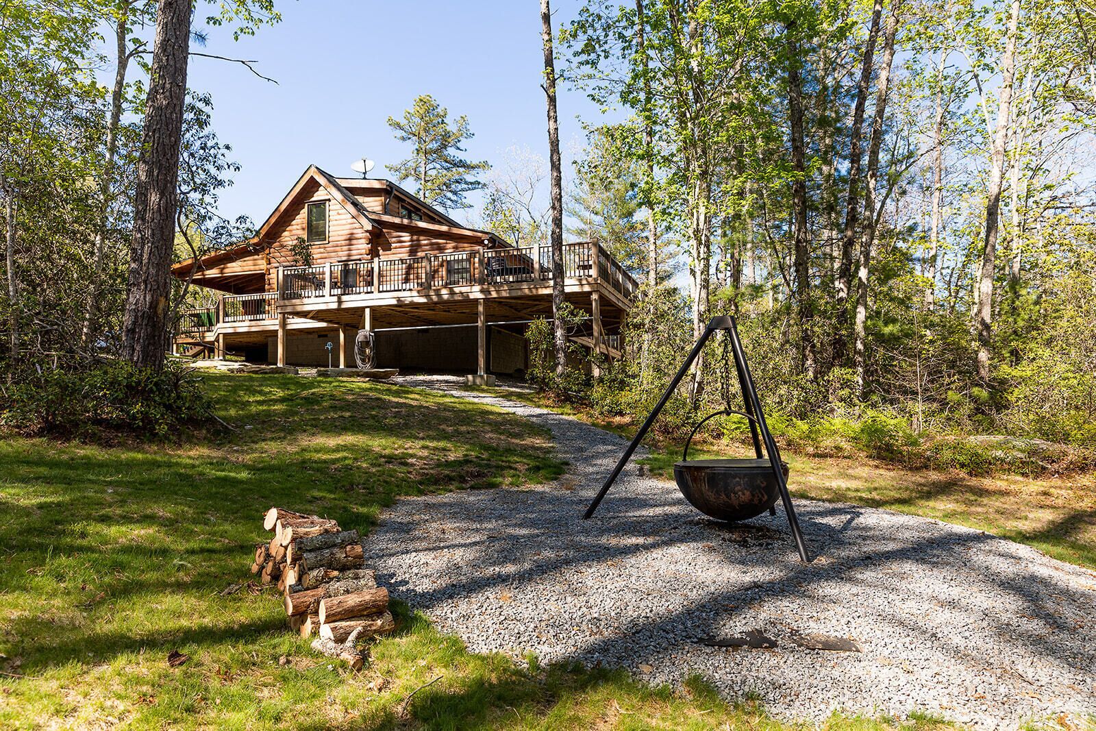 Eine Blockhütte mit einer Terrasse, umgeben von Bäumen und einem Kiesweg.