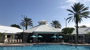 Une piscine entourée de palmiers et d’un bâtiment à toit de tuiles, avec des chaises longues et des parasols à proximité.