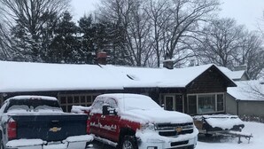 Zwei Lastwagen stehen auf einem verschneiten Einfahrt mit einem Haus im Hintergrund.