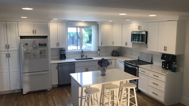 Una cocina moderna con armarios blancos, una isla central con taburetes, un horno empotrado y un microondas sobre la estufa.
