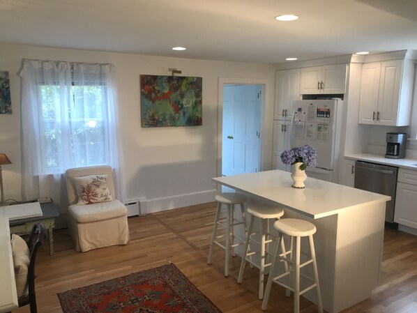 A modern kitchen with white cabinetry, a central island with stools, a coffee maker, and a refrigerator. - Miacomet Marvel with Pool and Cabana (Nantucket)