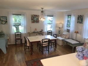 A dining area with a white table and chairs, a chandelier, and a window with curtains. - Miacomet Marvel with Pool and Cabana (Nantucket)
